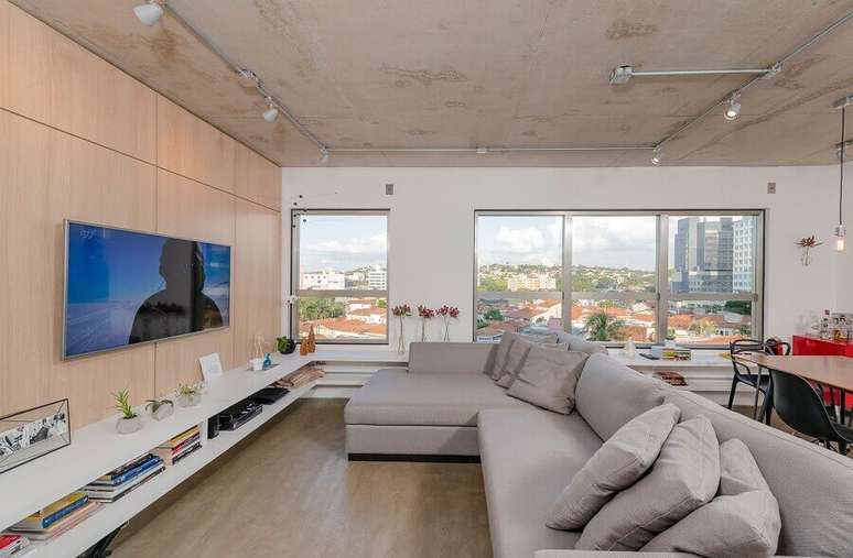 28. Sala ampla decorada com TV na parede e sofá cinza com chaise – Foto: Archdaily