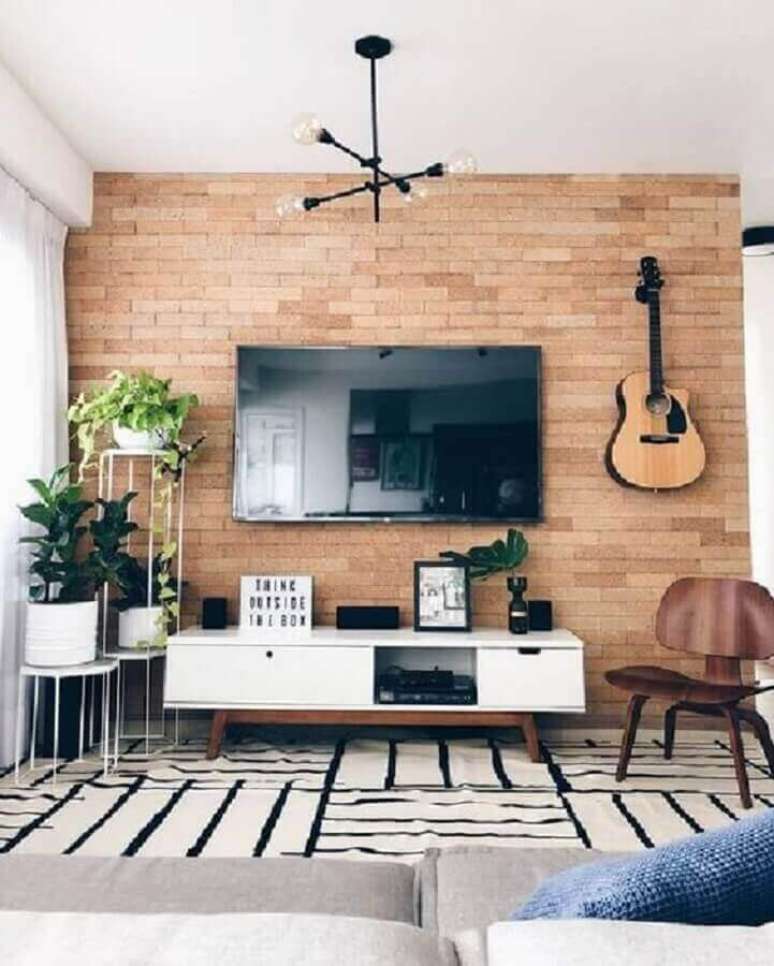 29. TV direto na parede de sala decorada com tapete preto e branco e vasos de plantas – Foto: Pinterest