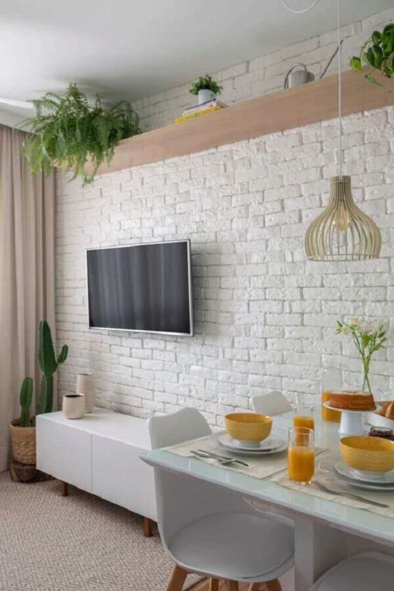 37. TV direto na parede de sala branca com rack retrô e vasos de plantas – Foto: Pinterest