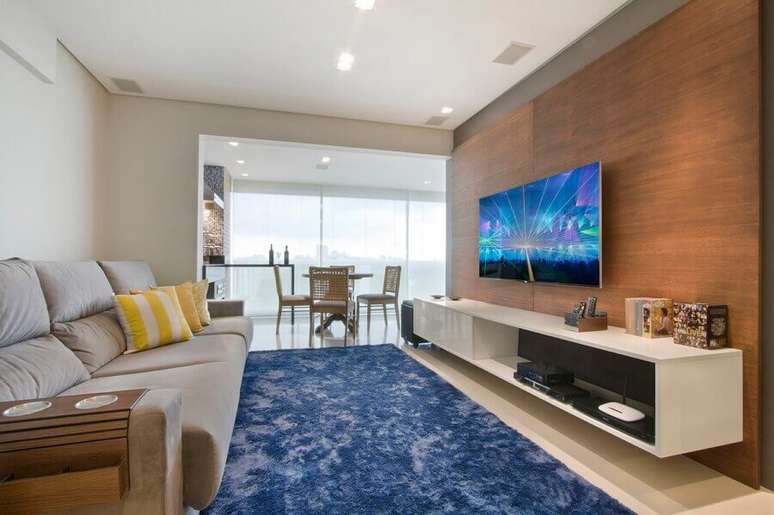 46. Painel de madeira como suporte para TV na parede de sala decorada com sofá cinza e tapete azul – Foto: Pinterest