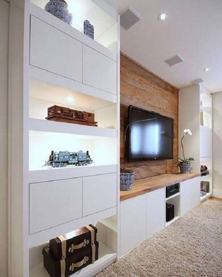 55. Decoração de sala planejada com estante branca e TV na parede com revestimento de madeira – Foto: Pinterest