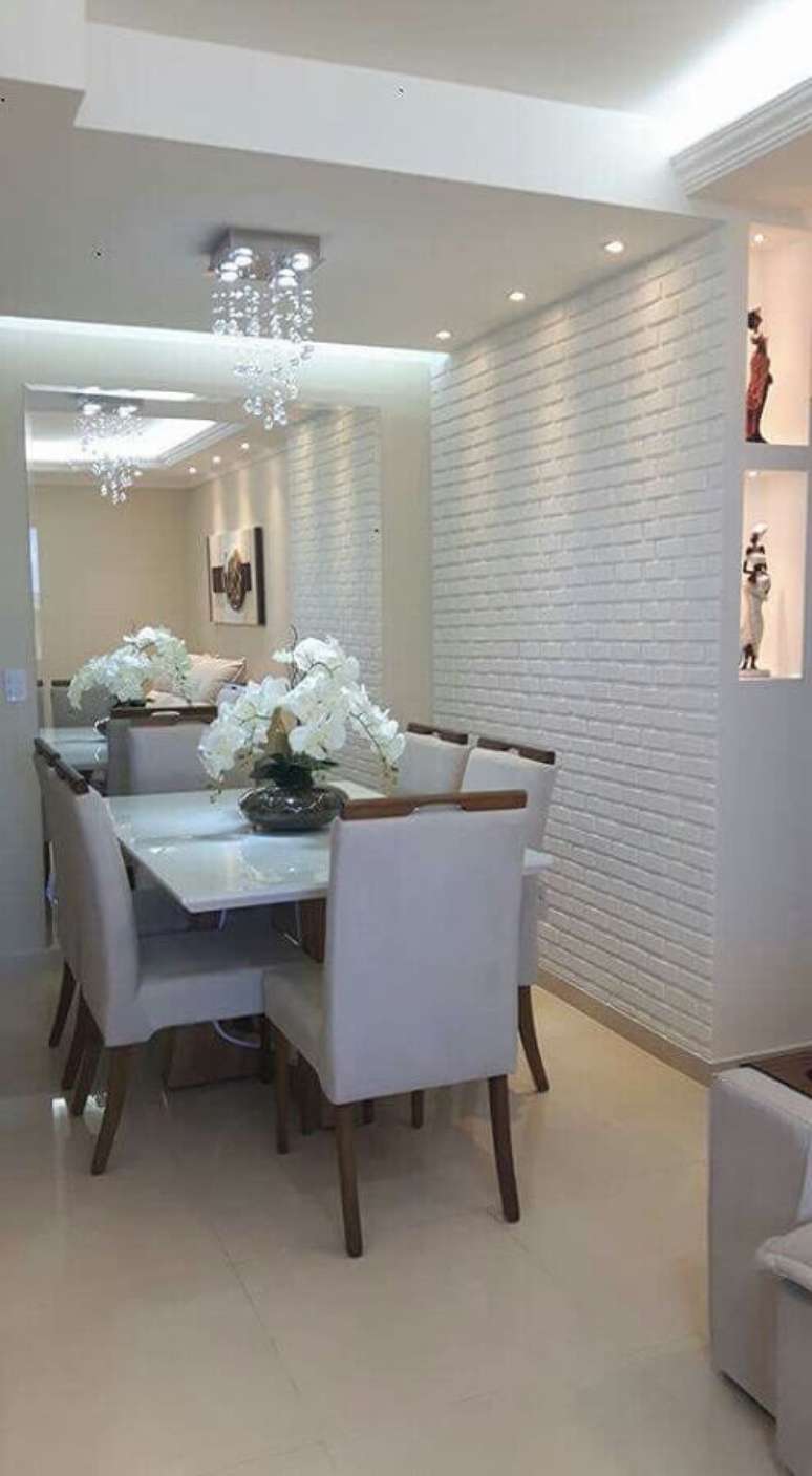 41. Sala de jantar branca decorada com lustre de cristal, espelho grande e papel de parede tijolinho branco – Foto: Manual da Obra