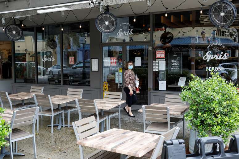 Mulher usando m&aacute;scara protetora passa por mesas vazias do lado de fora de um restaurante, enquanto o condado de Miami-Dade flexibiliza algumas das medidas de bloqueio colocadas em pr&aacute;tica durante o surto da doen&ccedil;a causada pelo coronav&iacute;rus, em Miami, Fl&oacute;rida, EUA, 18 de maio de 2020. REUTERS/Marco Bello