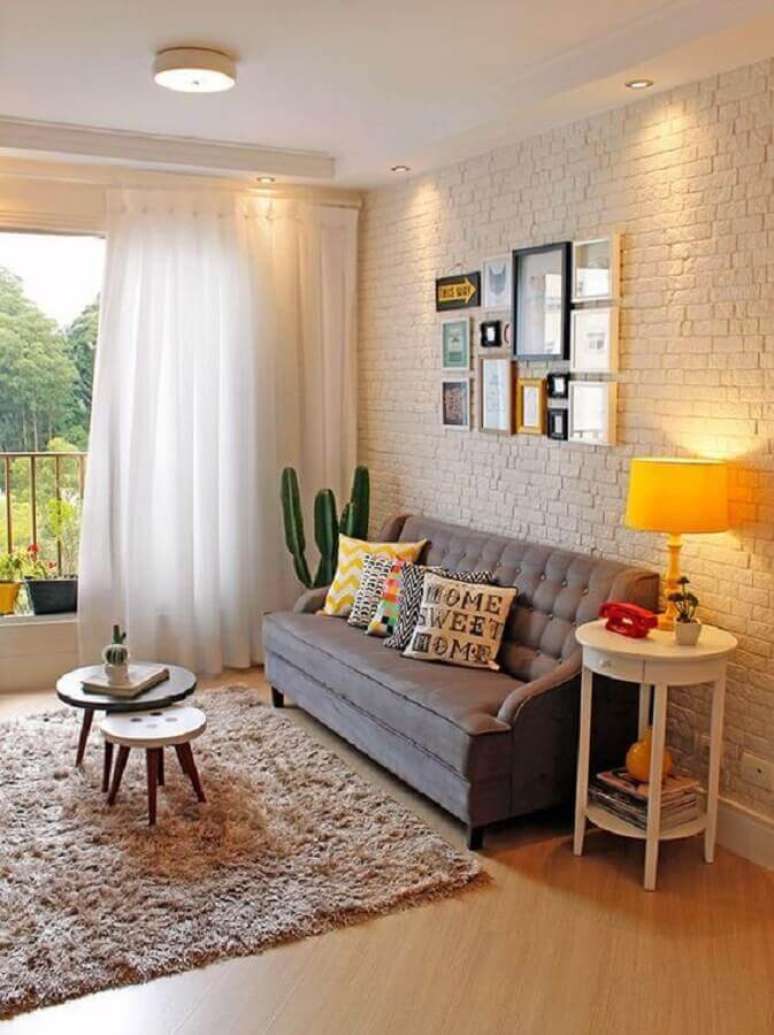 21. Mesa de canto redonda branca com gaveta para decoração de sala com sofá cinza e parede de tijolinho branco – Foto: Pinterest