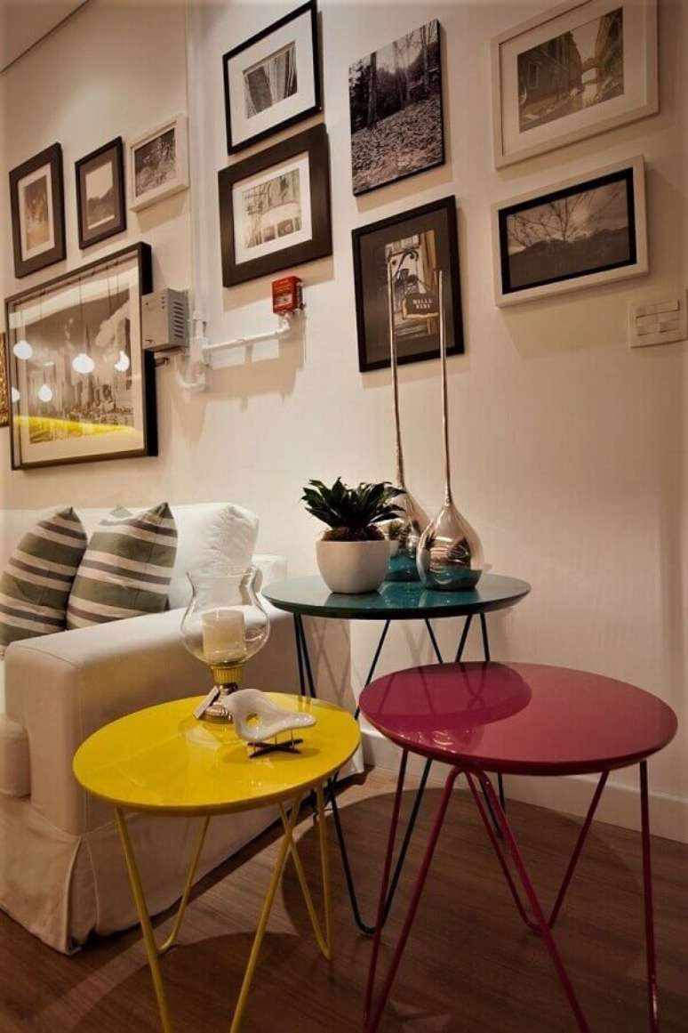 53. Sala branca decorada com vários quadros na parede e mesa de canto redonda amarela, rosa e verde – Foto: