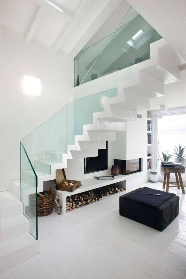 23. Decoração clean e moderna para casa com guarda-corpo de vidro e lareira embaixo da escada – Foto: Pinterest