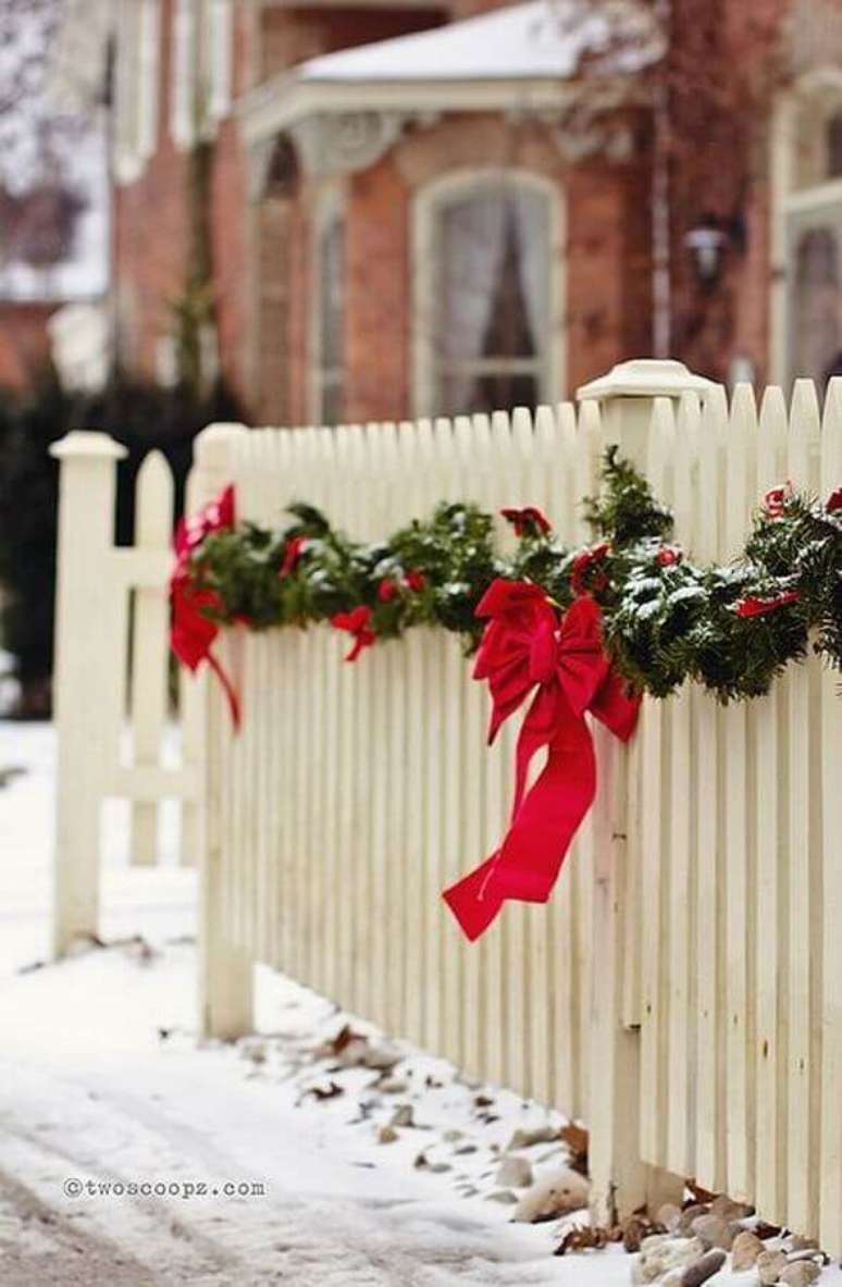 39. Cerca branca de casa decorada com festão de Natal verde decorado com laços vermelhos – Foto: Trend4Homy