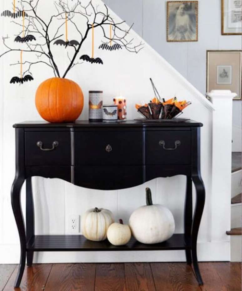 33. A abóbora de halloween sobre a cômoda preta serve de vaso para galhos secos. Fonte: Pinterest
