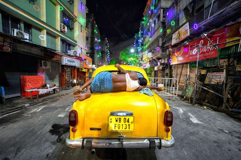 Motorista de táxi dormindo em cima de seu carro em Calcutá