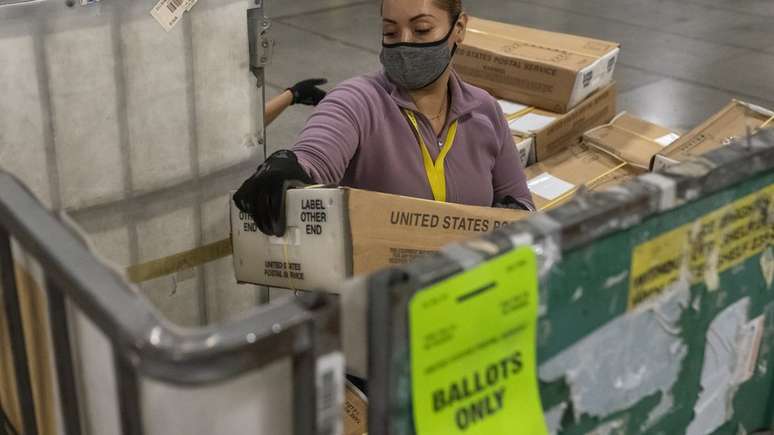 Funcionária do serviço postal carrega caixa lotada de votos no Estado do Oregon