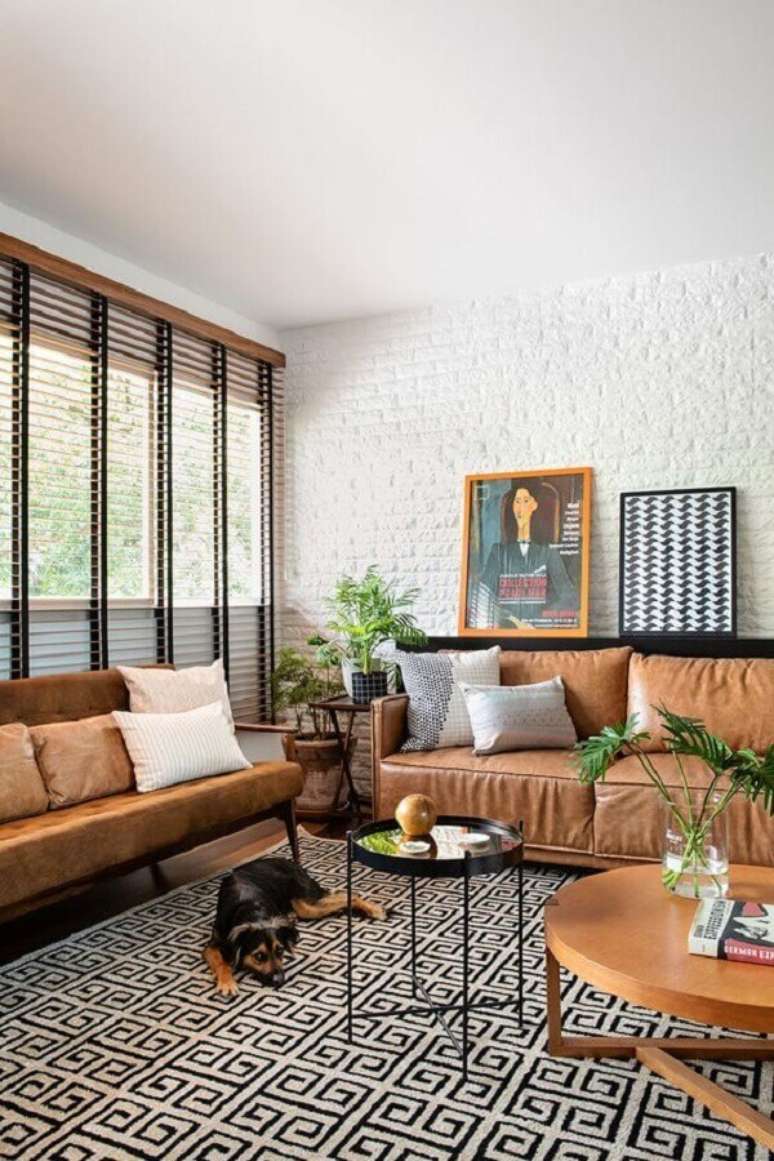 46. Sofá de couro para decoração de sala com tapete geométrico e parede de tijolinho branca – Foto: Casa de Valentina