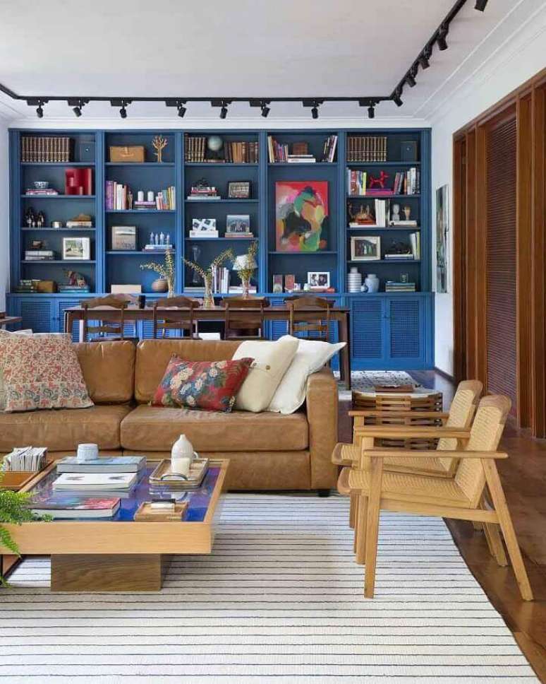 64. Sof&aacute; marrom claro para decora&ccedil;&atilde;o de sala com estante planejada azul e poltronas de madeira &ndash; Foto: Adriana Valle e Patr&iacute;cia Carvalho