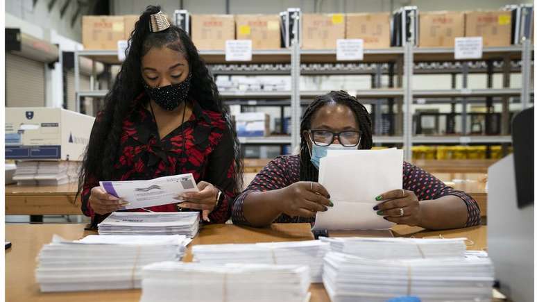 Trabalhando em duplas bipartidárias, funcionárias processam votos pelo correio no Estado de Maryland, o primeiro a começar a processar os votos remotos no país
