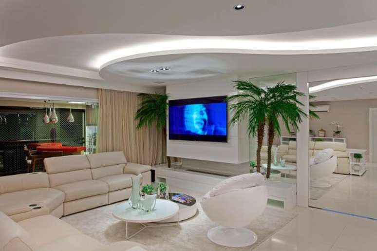 58. Ambiente com decoração clean com parede espelhada e mesa de centro redonda branca. Fonte: Iara Kilaris