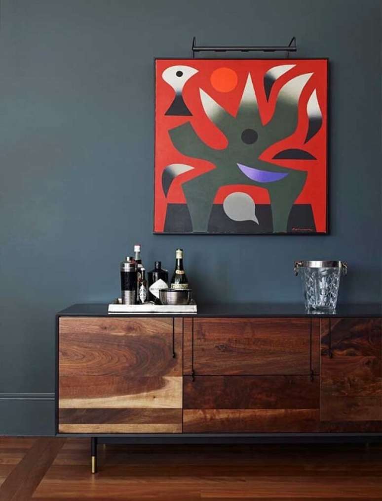 59. A parede azul petr&oacute;leo recepciona muito bem o quadro colorido. Fonte: Pinterest