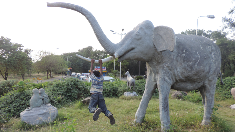 Um menino se balançando em uma estátua de elefante na avenida fora do zoológico de Islamabad