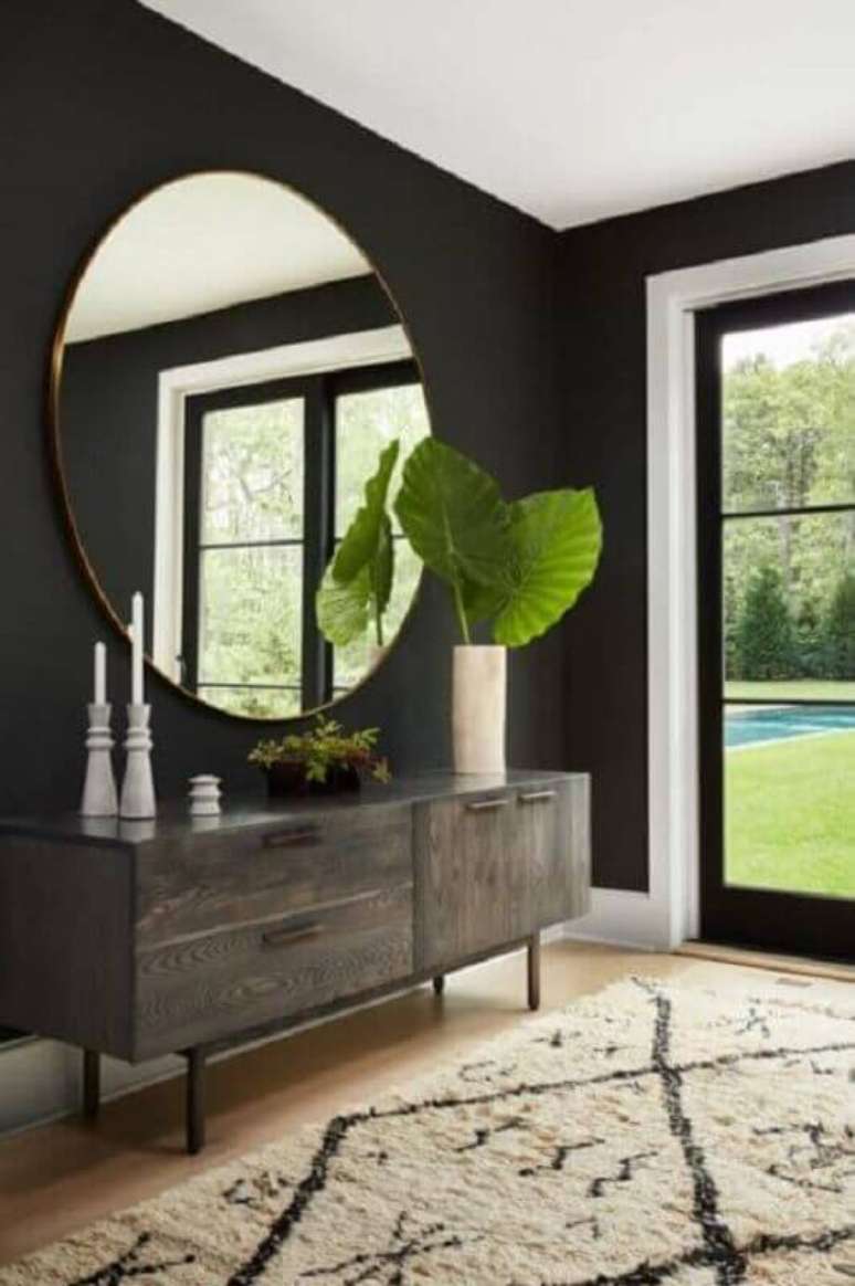 39. Hall de entrada preto decorado com espelho grande redondo e buffet de madeira &ndash; Foto: Apartment Therapy