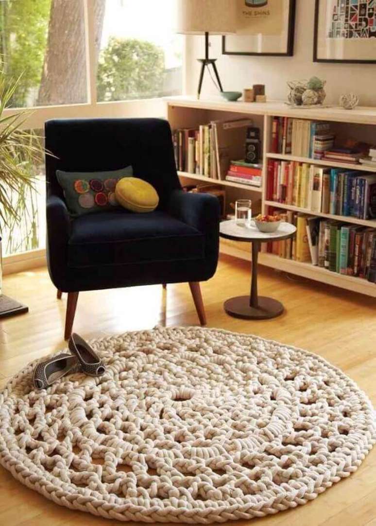 7. Tapete de croch&ecirc; bege redondo para sala decorada com estante de livros e poltrona azul marinho &ndash; Foto: Muito Chique