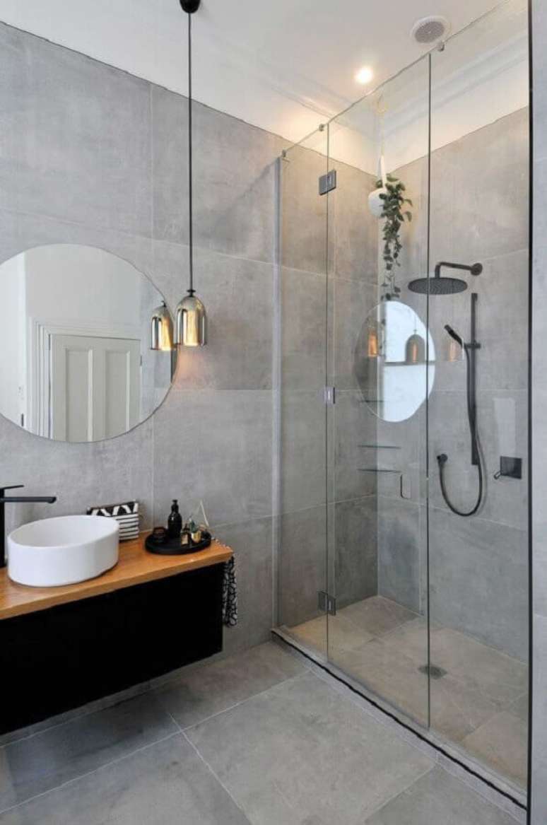 24. Tons de cinza para parede de banheiro moderno decorado com espelho redondo e gabinete suspenso preto com bancada de madeira – Foto: Apartment Therapy