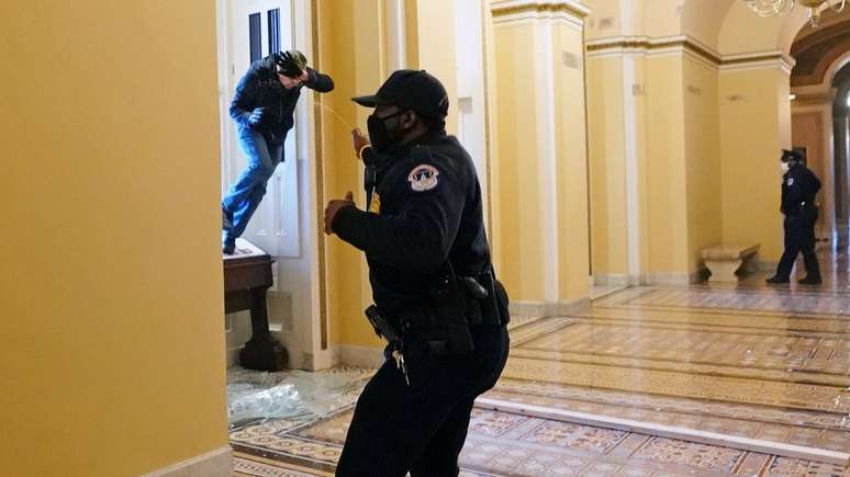 Um policial do Capitólio dos EUA atira spray de pimenta em um protesto entrando no prédio por uma janela quebrada