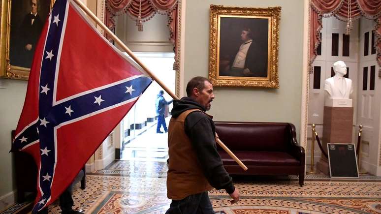 Manifestante carrega a bandeira da Confederação ao invadir o Capitólio dos EUA