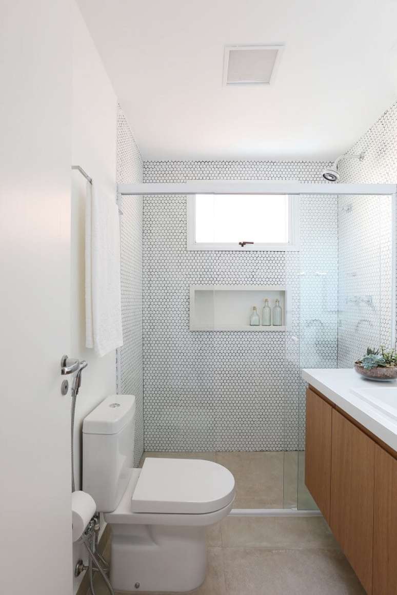38. Banheiro clean com chuveiro cromado e balcão com portas de madeira. Projeto por Livia Dalmaso