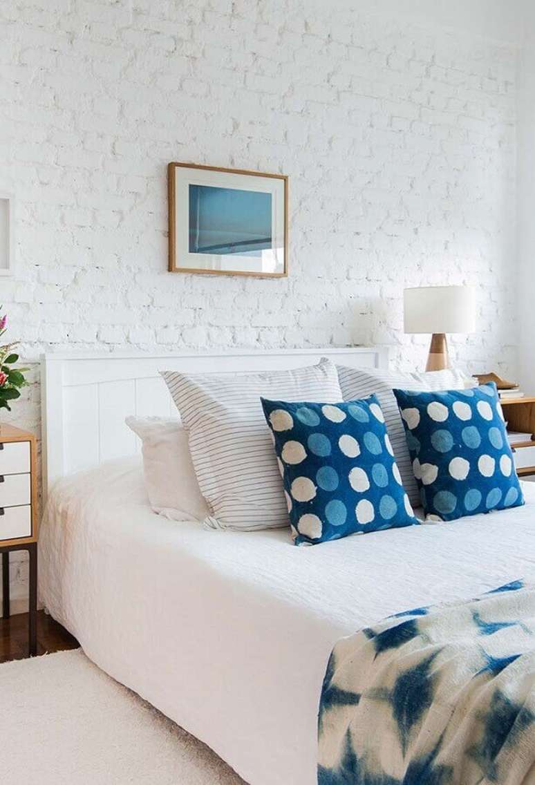 8. Cores claras para quarto de casal com parede de tijolinho branca e almofadas azuis – Foto: Sua Decoração