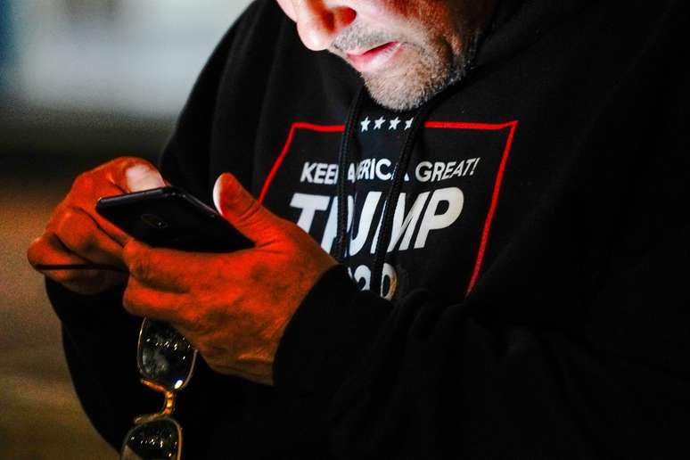 Homem usando camiseta escrita "Trump 2020" confere seu telefone celular durante protesto em Milwaukee. 5/11/2020. REUTERS/Bing Guan