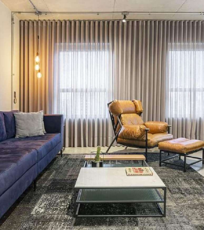37. Poltrona de couro caramelo para sala moderna decorada com tapete cinza e sofá azul – Foto: Jeito de Casa