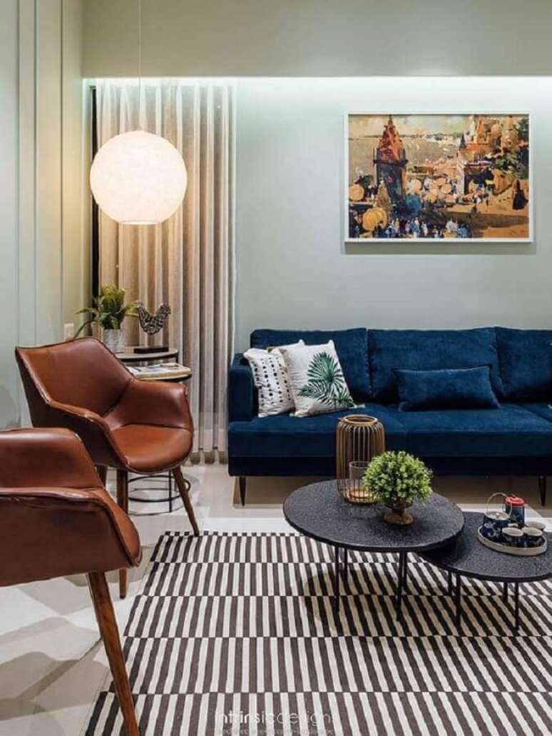 45. Poltrona de couro marrom para sala de estar decorada com sofá azul escuro e tapete listrado – Foto: Horchow