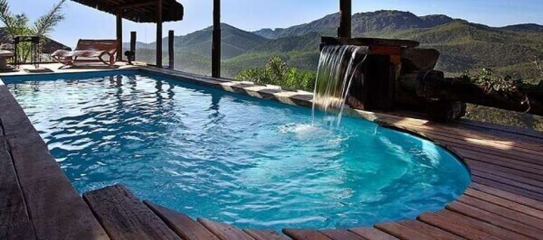 42- O acabamento da cascata para piscina &eacute; realizada com pedras e madeira. Fonte: Pinterest