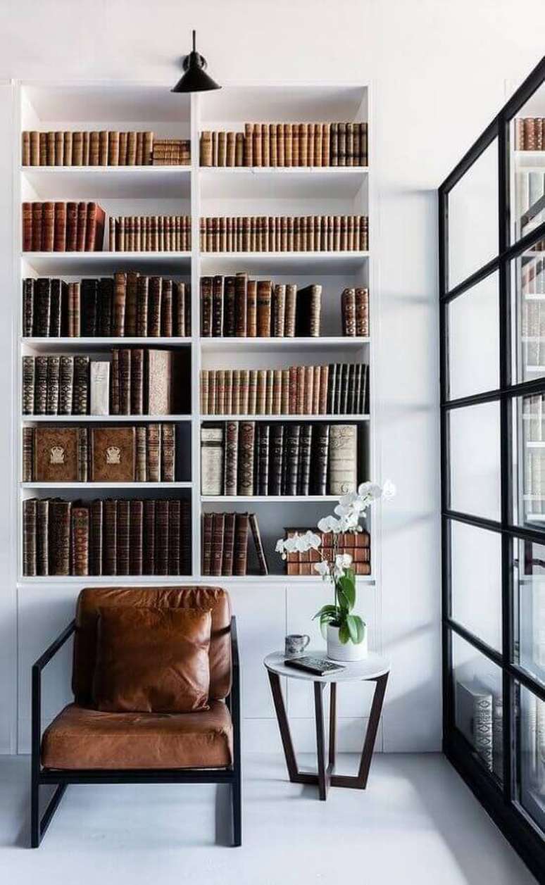 8. Decoração minimalista com estante branca planejada e poltrona de couro para leitura – Foto: Futurist Architecture