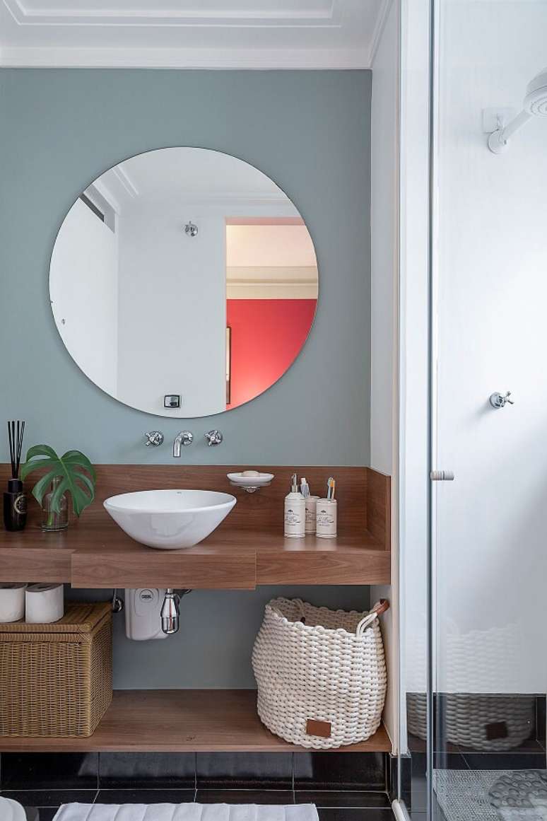 9. Parede com pintura cinza se conecta com a bancada em madeira e a cuba de apoio oval para banheiro branca. Projeto por Batistelli Arquitetura e Design