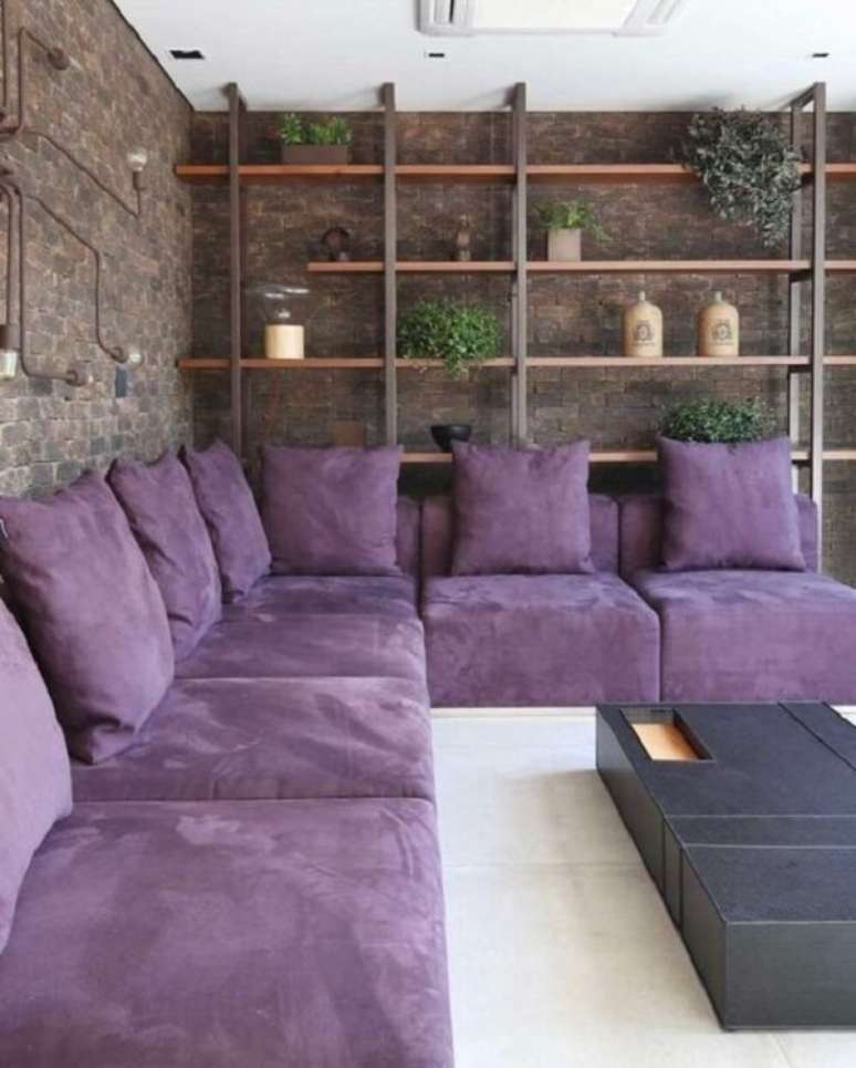 52. Sala contempor&acirc;nea com sof&aacute; de canto roxo e parede de tijolinho aparente. Fonte: Pinterest