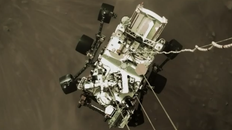 Robô Perseverance quando estava pousando em Marte, visto do foguete que auxiliou em sua descida