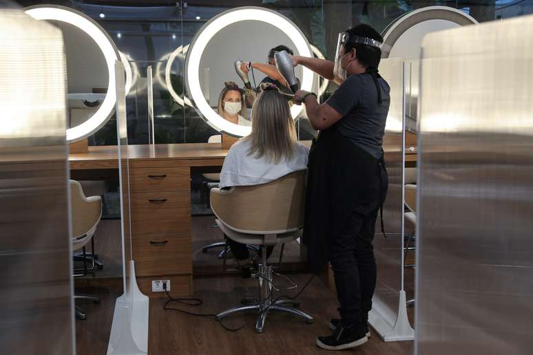 A hairdresser wearing protective mask and face shield uses a hair dryer on a customer's hair between acrylic walls set up for social distancing at a hair salon, as the city eases the restrictions imposed to control the spread of the coronavirus disease (COVID-19), in Sao Paulo, Brazil July 6, 2020. REUTERS/Amanda Perobelli