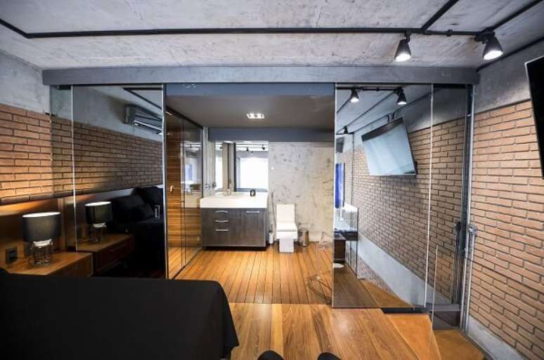 8. Parede de tijolinho aparente e porta para quarto de correr espelhada marcam a decora&ccedil;&atilde;o do espa&ccedil;o. Fonte: Carla Cuono Arquitetura e Interiores
