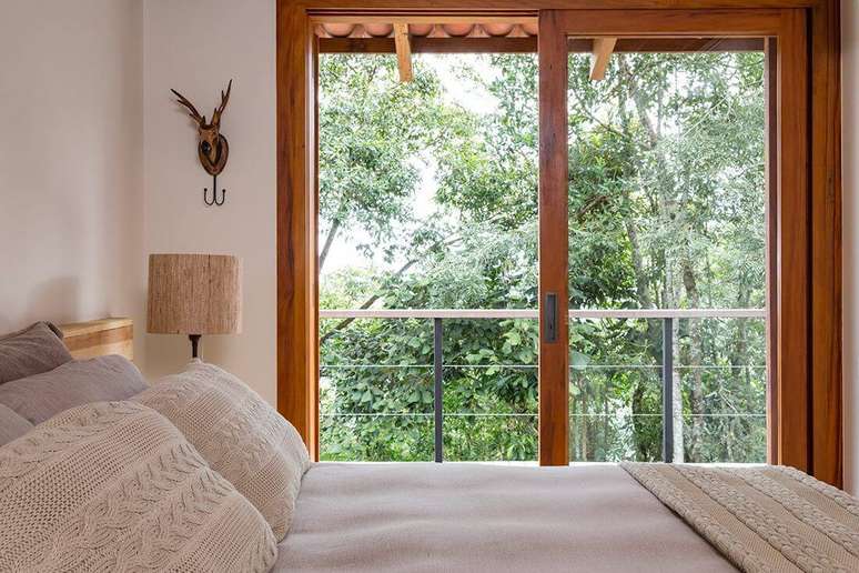 47. A porta de correr para quarto de vidro com acabamento em madeira permite a vis&atilde;o da paisagem do entorno do im&oacute;vel. Fonte: RAP Arquiteutra e Interiores