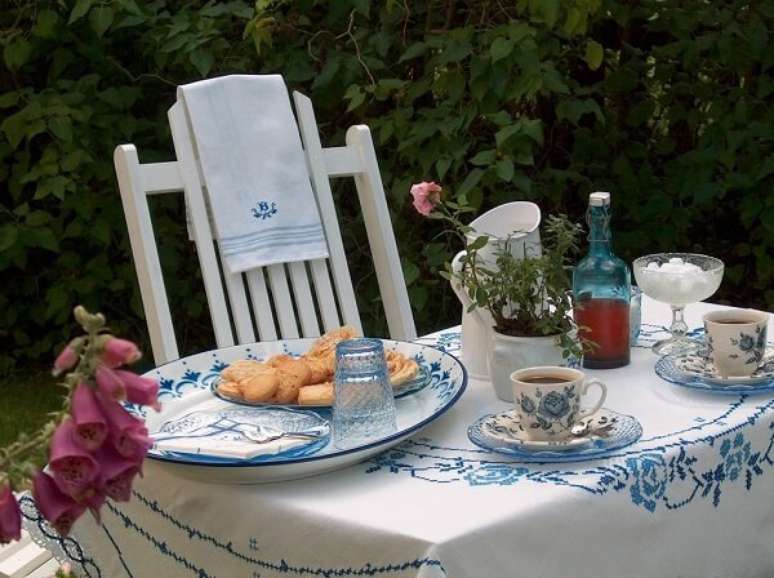 55- A mesa posta para o café da manhã tem toalha bordada em ponto cruz azul no mesmo tom da estampa da louça. Fonte: Ao Redor da Mesa