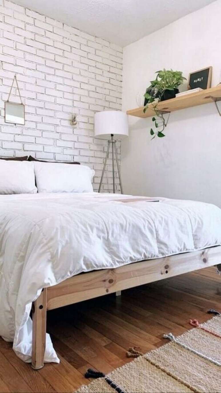 35. Decoração de quarto de casal simples com parede de tijolinho branco e cama de madeira – Foto EstiloyDeco