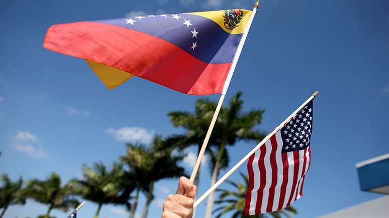 Uma pessoa segura duas bandeiras, dos Estados Unidos e da Venezuela