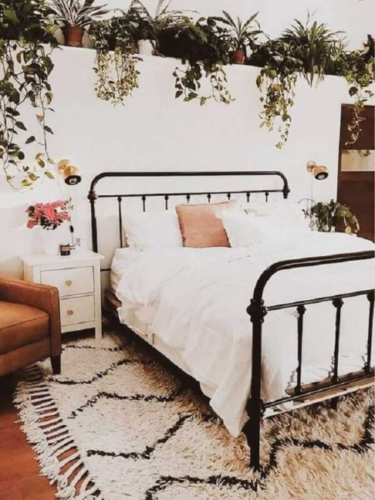 56. Quarto romântico decorado com vários vasos de plantas, cama de ferro e mesa de cabeceira retrô branca com gavetas. Fonte: A Casa Delas