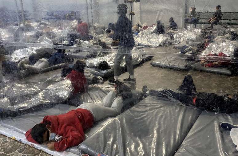 Jovens migrantes na instalação são mantidos em áreas lotadas separadas por lonas de plástico