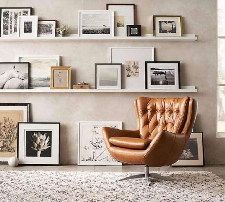 43. Poltrona marrom giratória para sala decorada com prateleiras para quadros – Foto: Pinterest