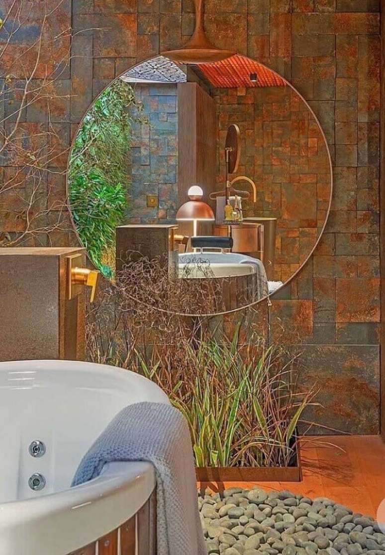 9. Decoração de banheiro com banheira, espelho redondo e revestimento de pedra ferro. Fonte: Mister Cryl Tintas