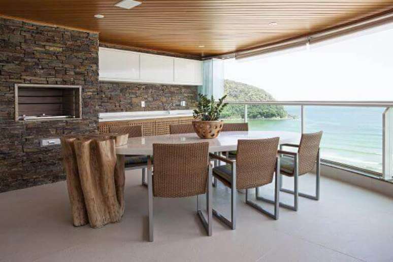 4. Arm&aacute;rio a&eacute;reo porta basculante e revestimento de parede em pedra decoram a varanda com churrasqueira. Fonte: Korman Arquitetos