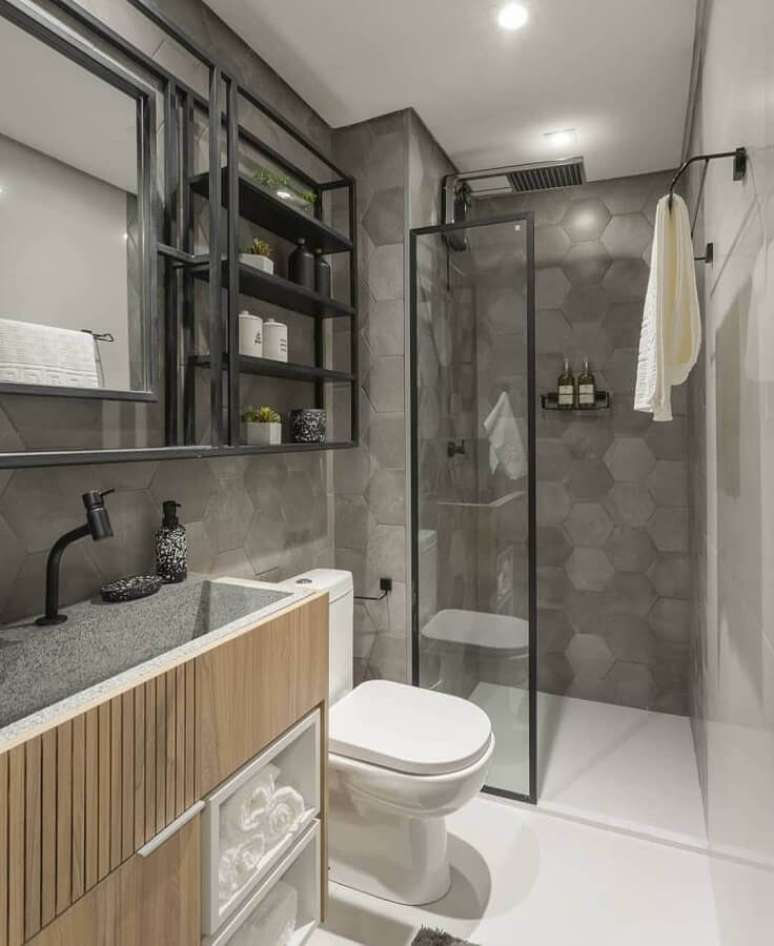 30. Decoração de banheiro moderno com gabinete de madeira e revestimento cinza hexagonal – Foto: Jeito de Casa