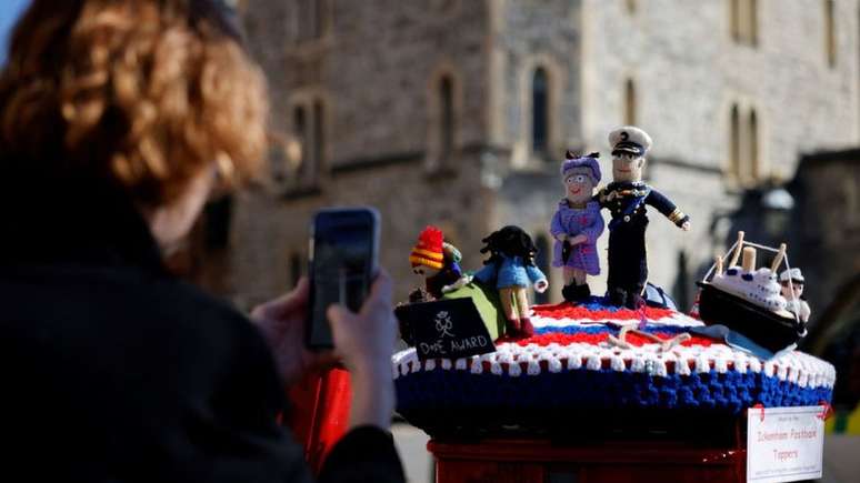 Mulher tira foto de bonequinhos de crochê feitos em homenagem à rainha e ao príncipe
