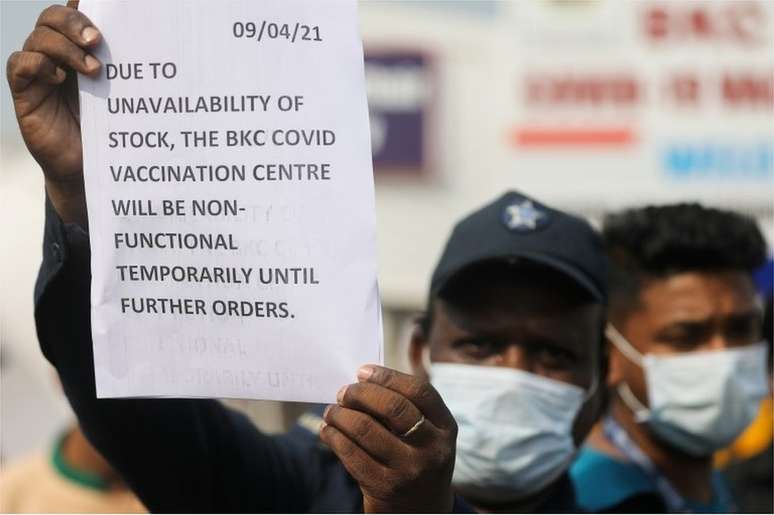 Um guarda segura um aviso para informar às pessoas sobre a escassez de suprimentos de vacina contra o coronavírus