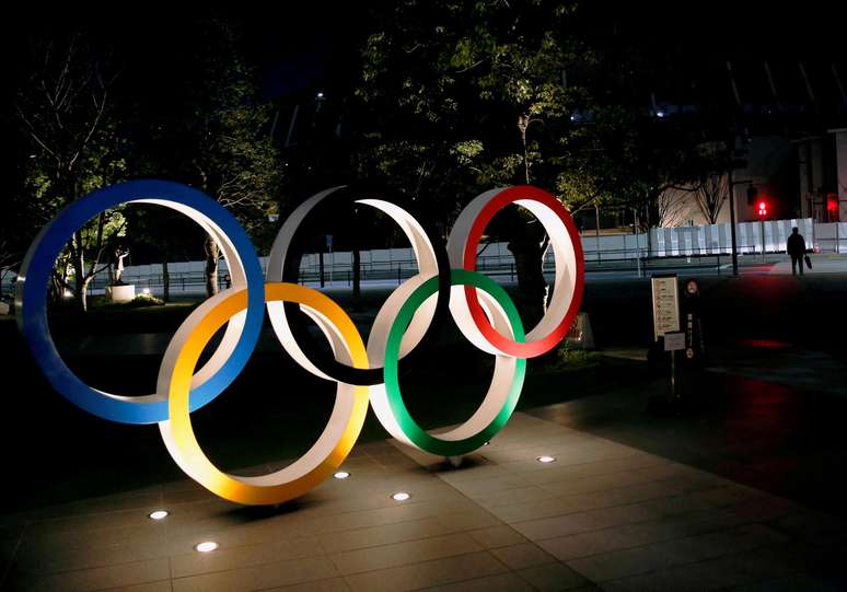 Os anéis olímpicos são iluminados em frente ao Estádio Nacional de Tóquio, no Japão